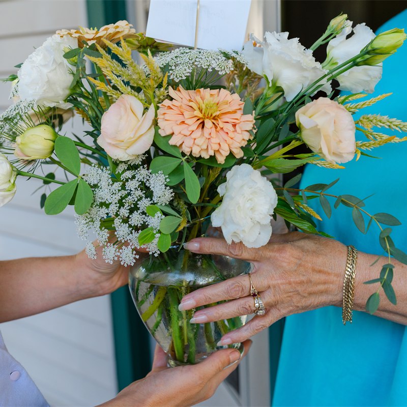 Close-up of a vase of peach zinnias, white lisianthus and ammi being handed from the florist to the recipient